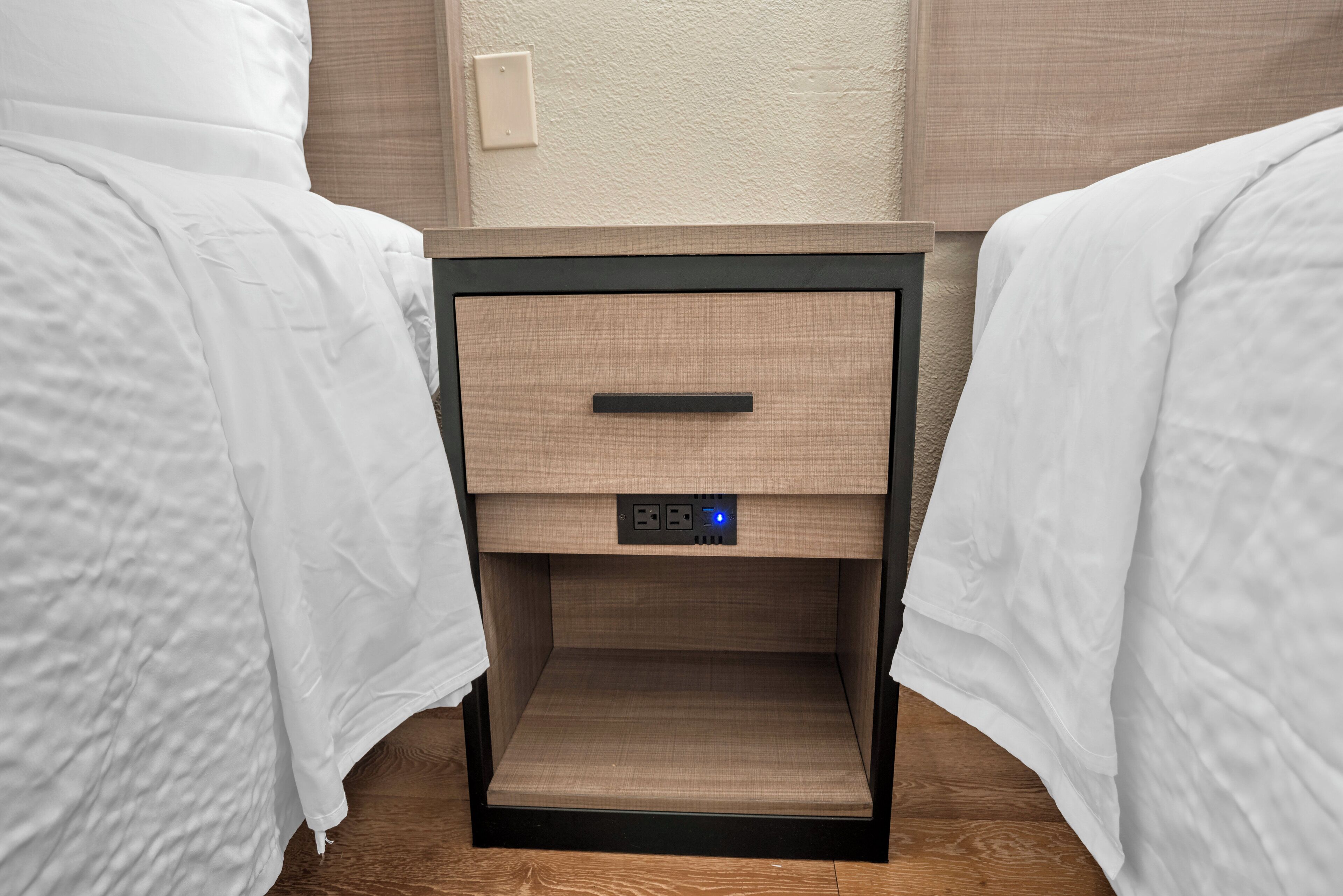 Una camera d'albergo con due letti singoli, un comodino con una sveglia digitale e una presa di corrente.