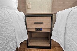 Habitación de hotel con dos camas individuales, una mesita de noche con un reloj digital y un enchufe.