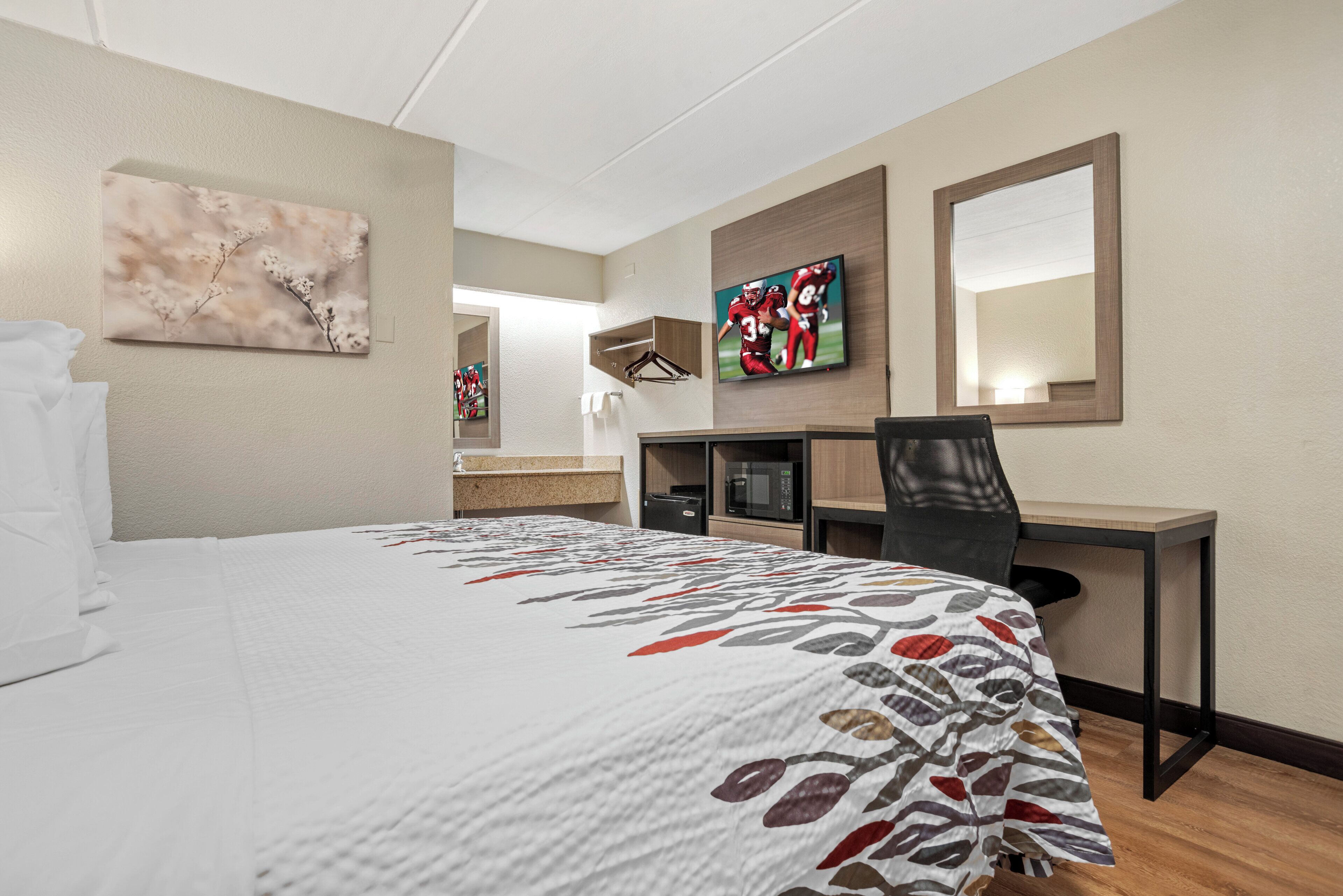 A hotel room with a bed, a desk, a chair, a television, and a mirror.