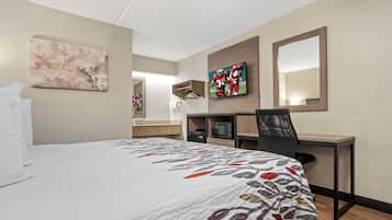 A hotel room with a bed, a desk, a chair, a television, and a mirror.