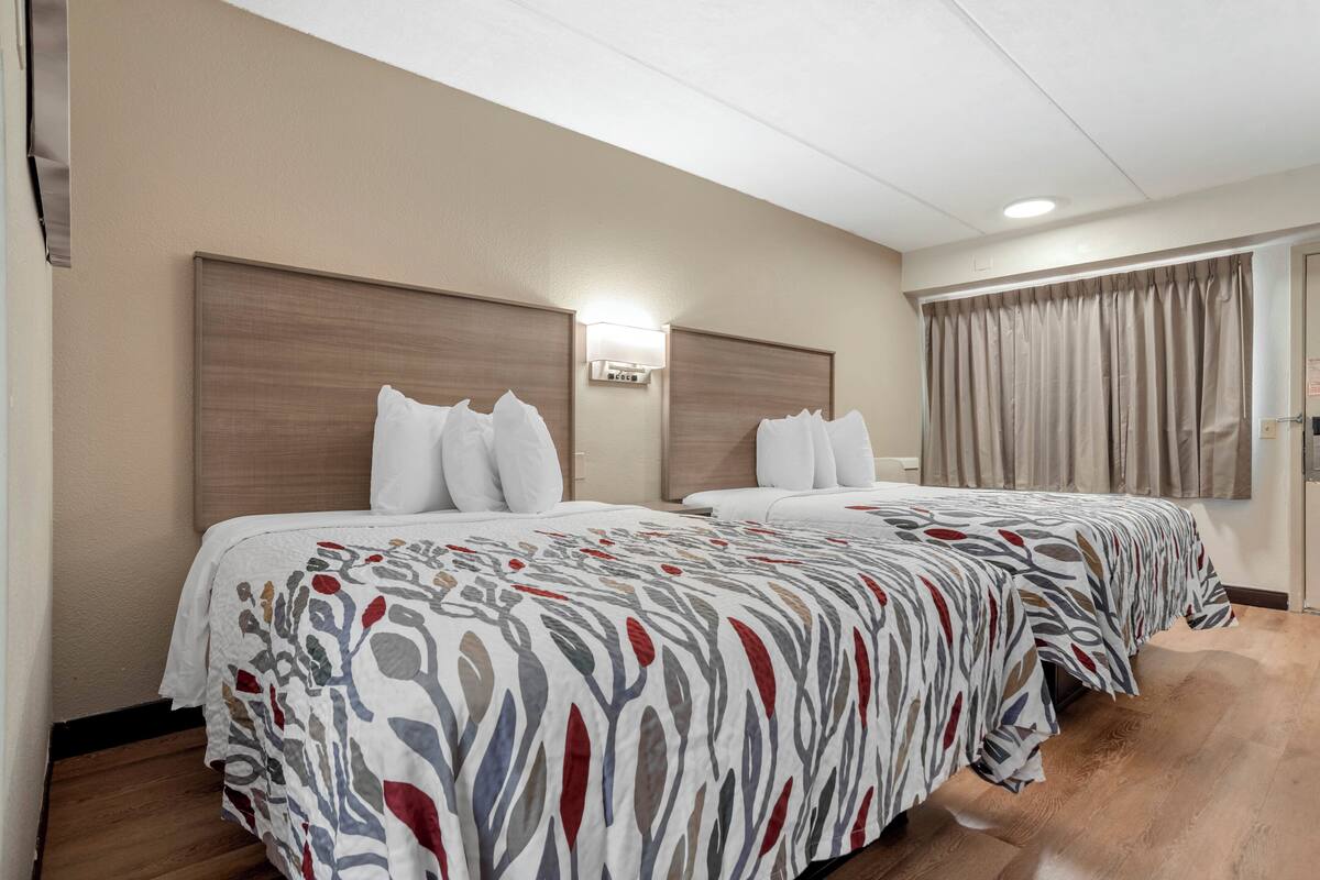 Een hotelkamer met twee bedden, een houten hoofdbord, een wandlamp en een raam met gordijnen.