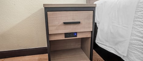 Une table de chevet en bois, dotée d’un tiroir, d’une prise électrique et d’une horloge numérique.