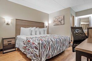 A hotel room with a bed, a nightstand, a chair, and a painting on the wall. - Red Roof Inn West Monroe (West Monroe)