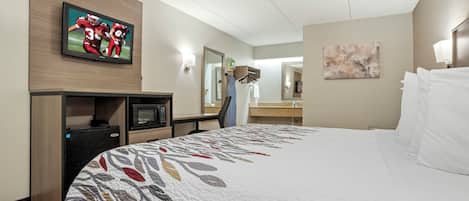 Quarto de hotel com cama, televisão, escrivaninha, espelho e um quadro na parede.