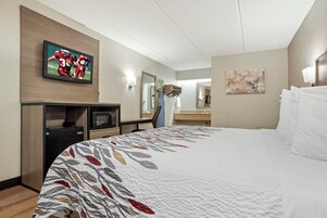 A hotel room with a bed, a television, a desk, a mirror, and a painting on the wall.