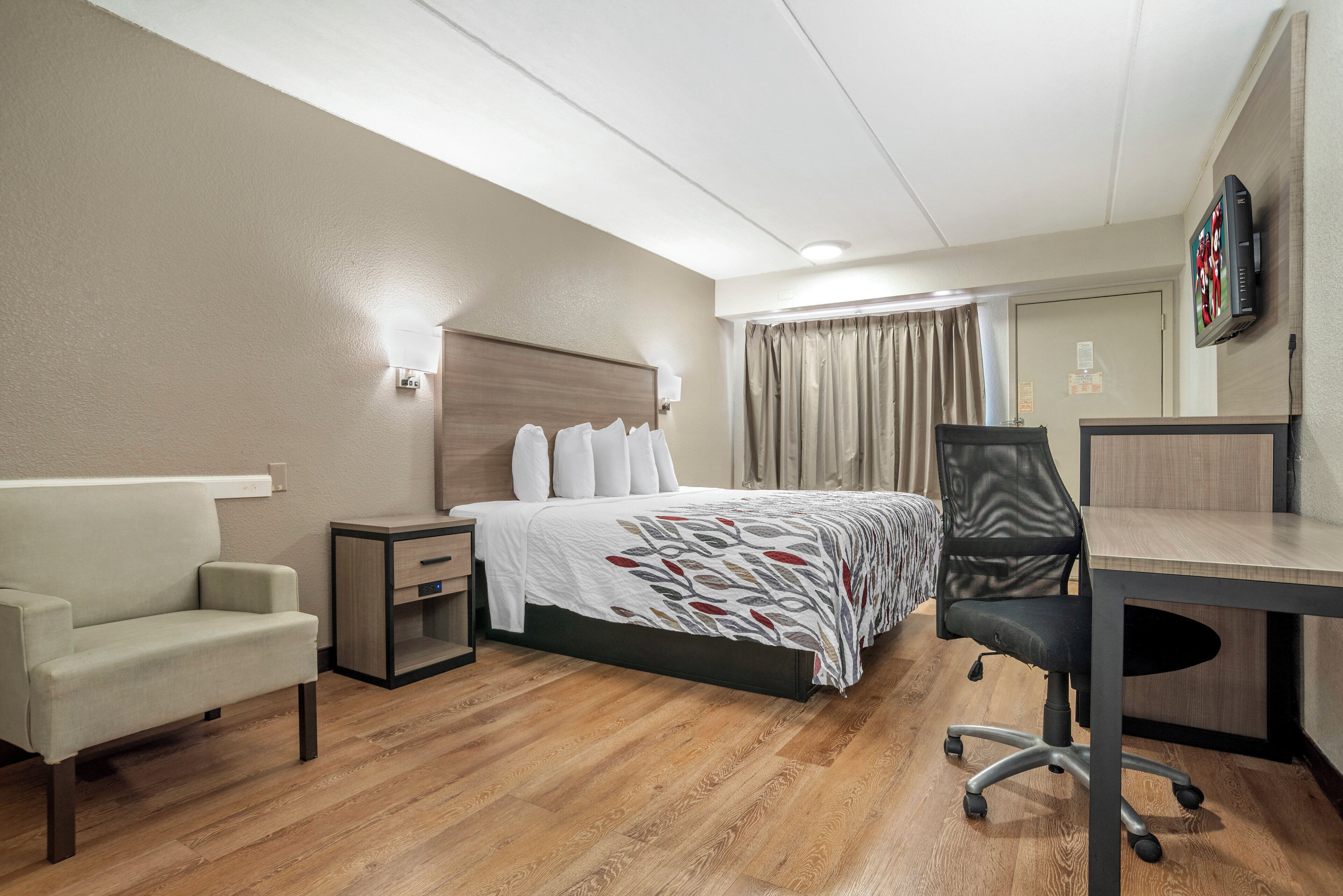 Ett hotellrum med en säng, ett skrivbord, en stol, en soffa och en tv.