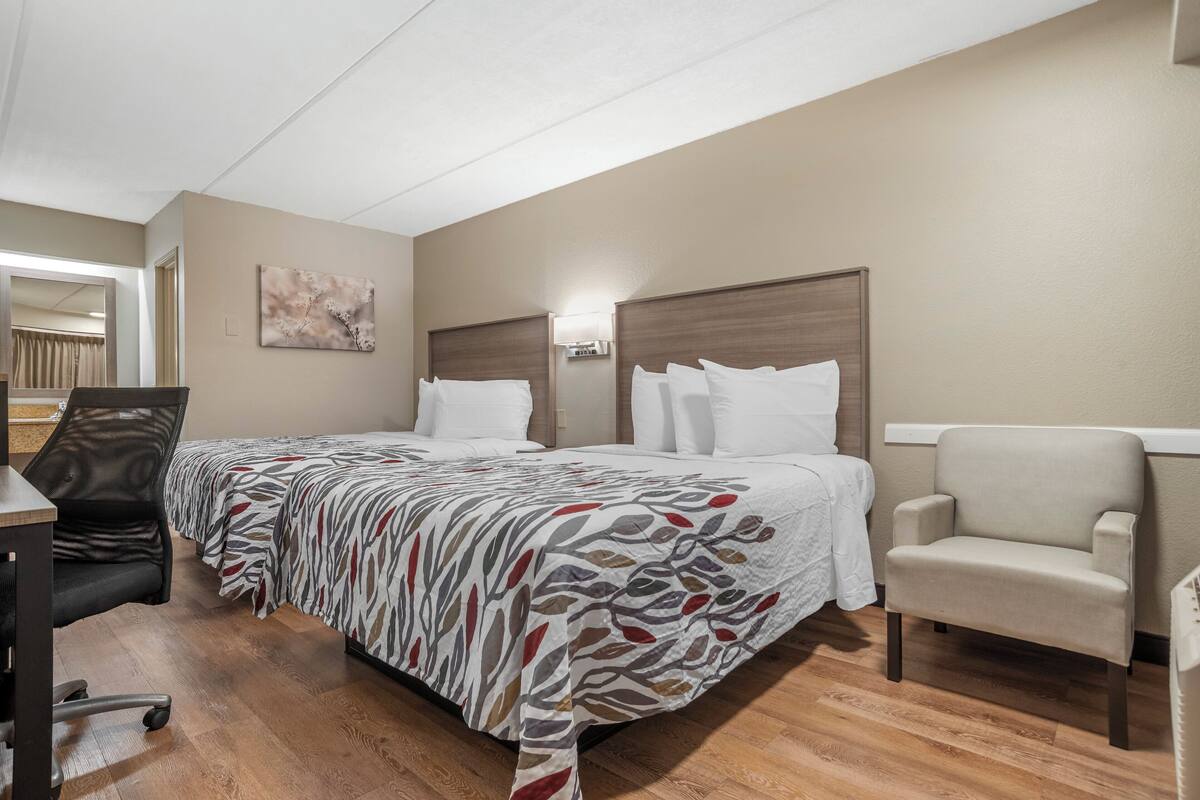 Een hotelkamer met twee bedden, een bureau, een stoel en een schilderij aan de muur.
