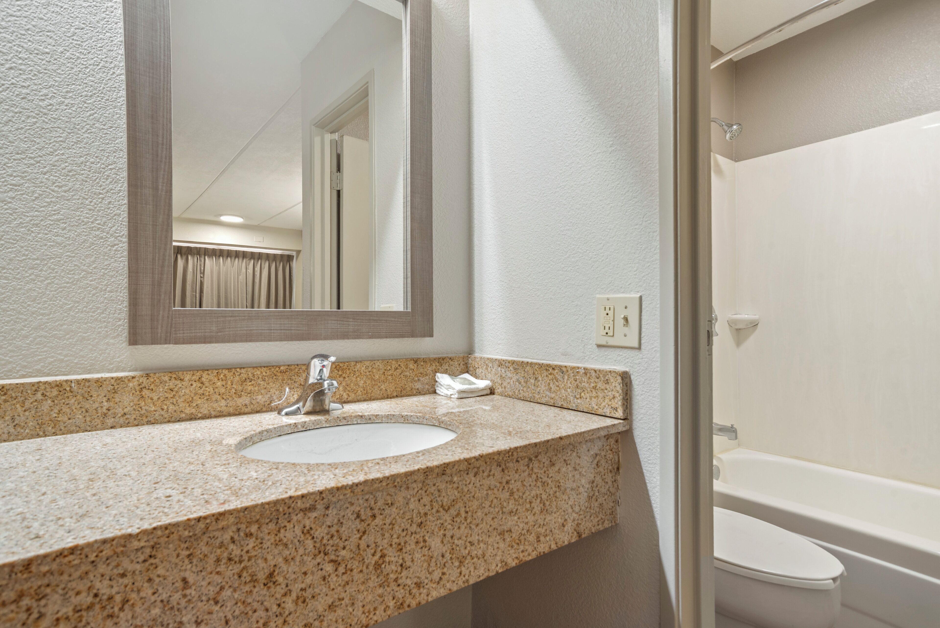 A bathroom with a granite countertop sink, a mirror, and a white bathtub.