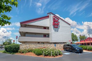 Un Red Roof Inn con una estructura de dos pisos, cimientos de piedra y un estacionamiento con un automóvil negro.