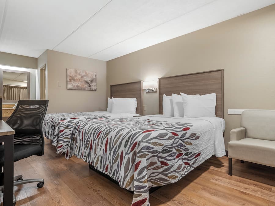 Quarto de hotel com duas camas, uma escrivaninha, uma cadeira e um quadro na parede.