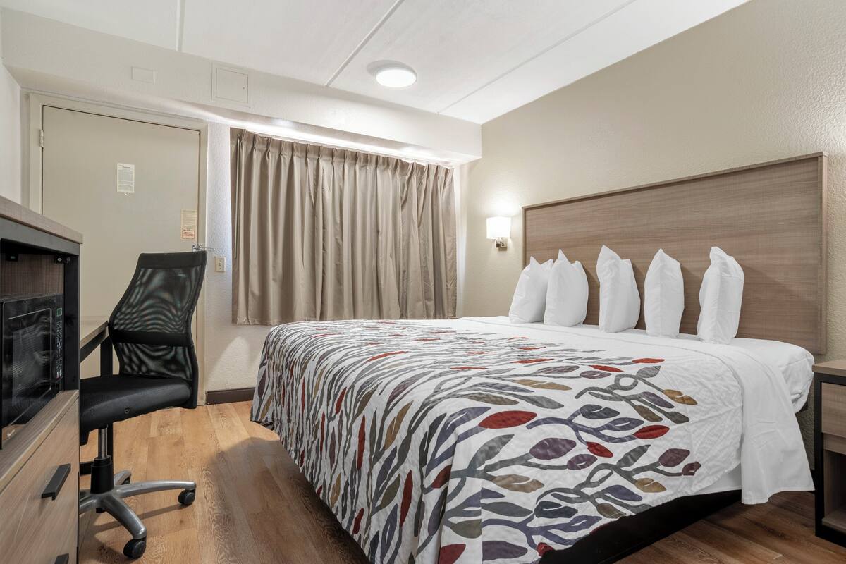 Hotelkamer met een bed, bureau met stoel, raam met gordijnen en een wandlamp.