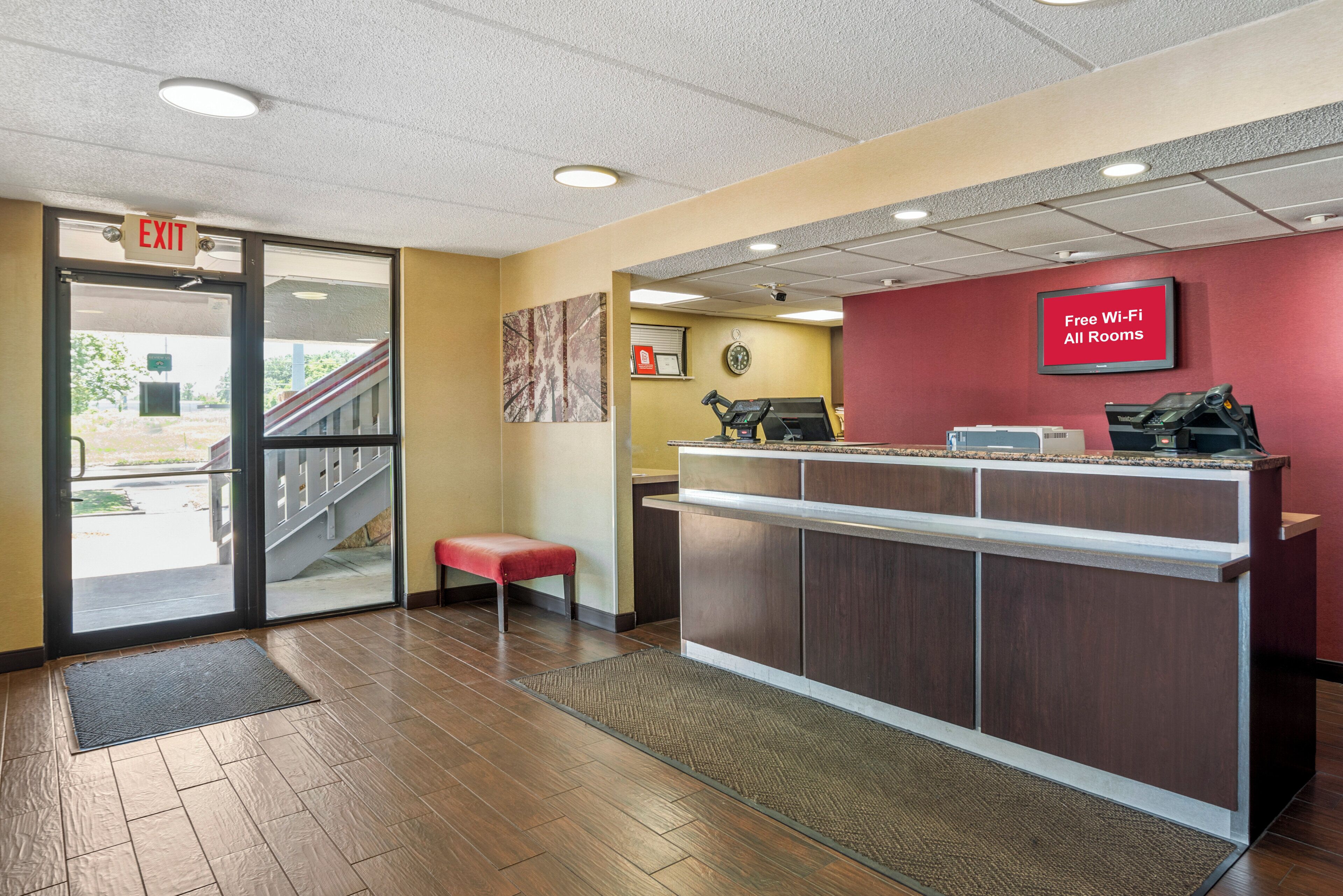 A reception area with a wooden floor, a reception desk, a red wall with a sign, and an exit door.