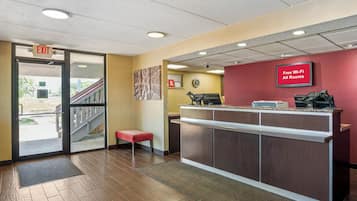 A reception area with a wooden floor, a reception desk, a red wall with a sign, and an exit door.