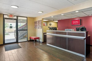 A reception area with a wooden floor, a reception desk, a red wall with a sign, and an exit door.