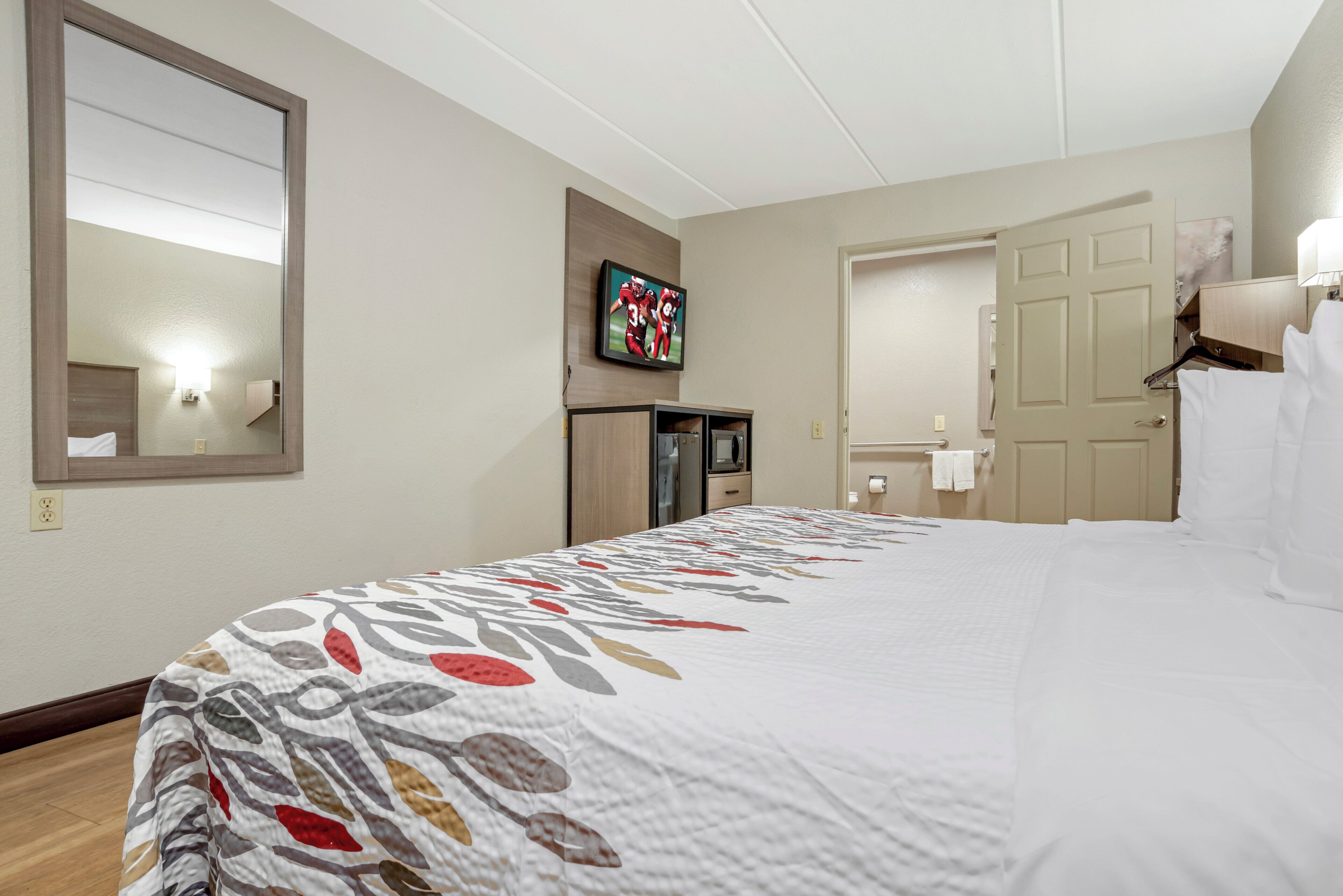 Una camera d'hotel con un letto grande, una televisione fissata al muro, una scrivania con un computer e un'apertura che dà su un bagno.