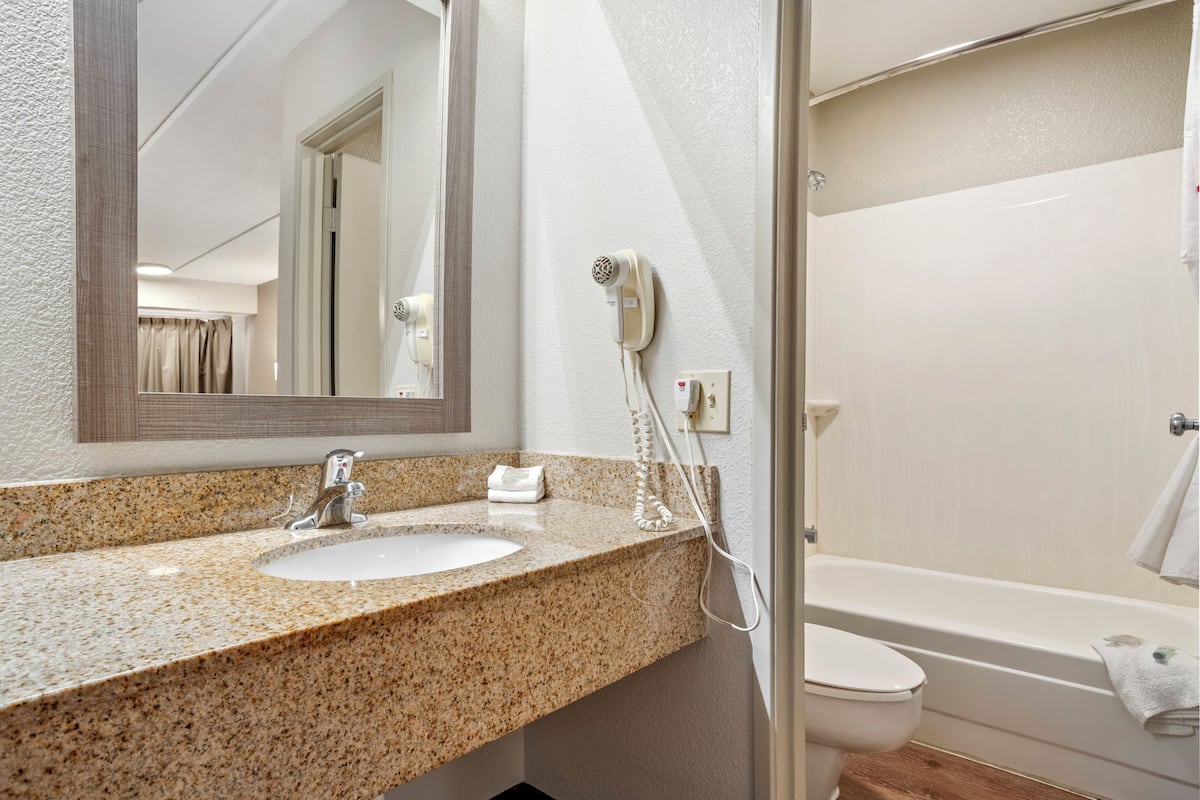 Un baño con lavamanos de granito, un espejo, secador de pelo y bañera.