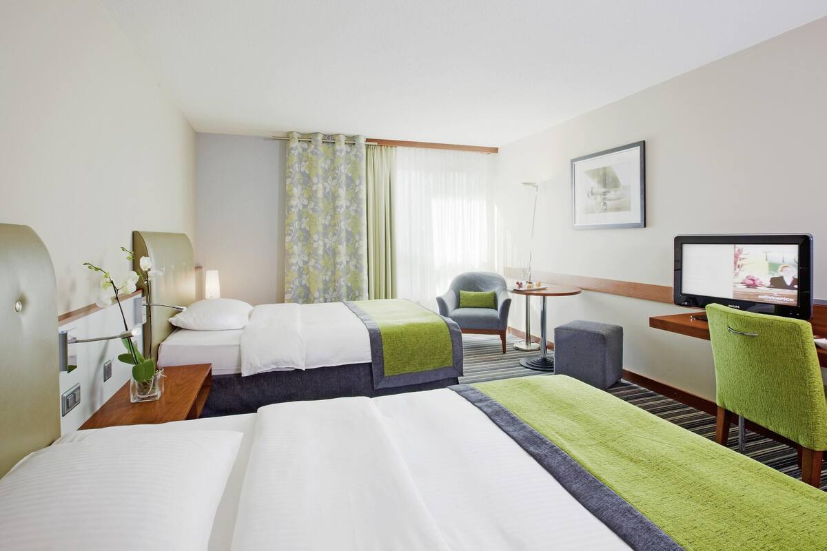 A hotel room with a large bed, two bedside tables, a desk with a chair, a television, and a window with curtains.