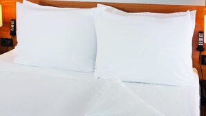 A neatly made bed with white linens and two pillows, a bedside table with a phone and a lamp, and a wooden headboard. - Mövenpick Hotel Zuerich-Airport (Opfikon)