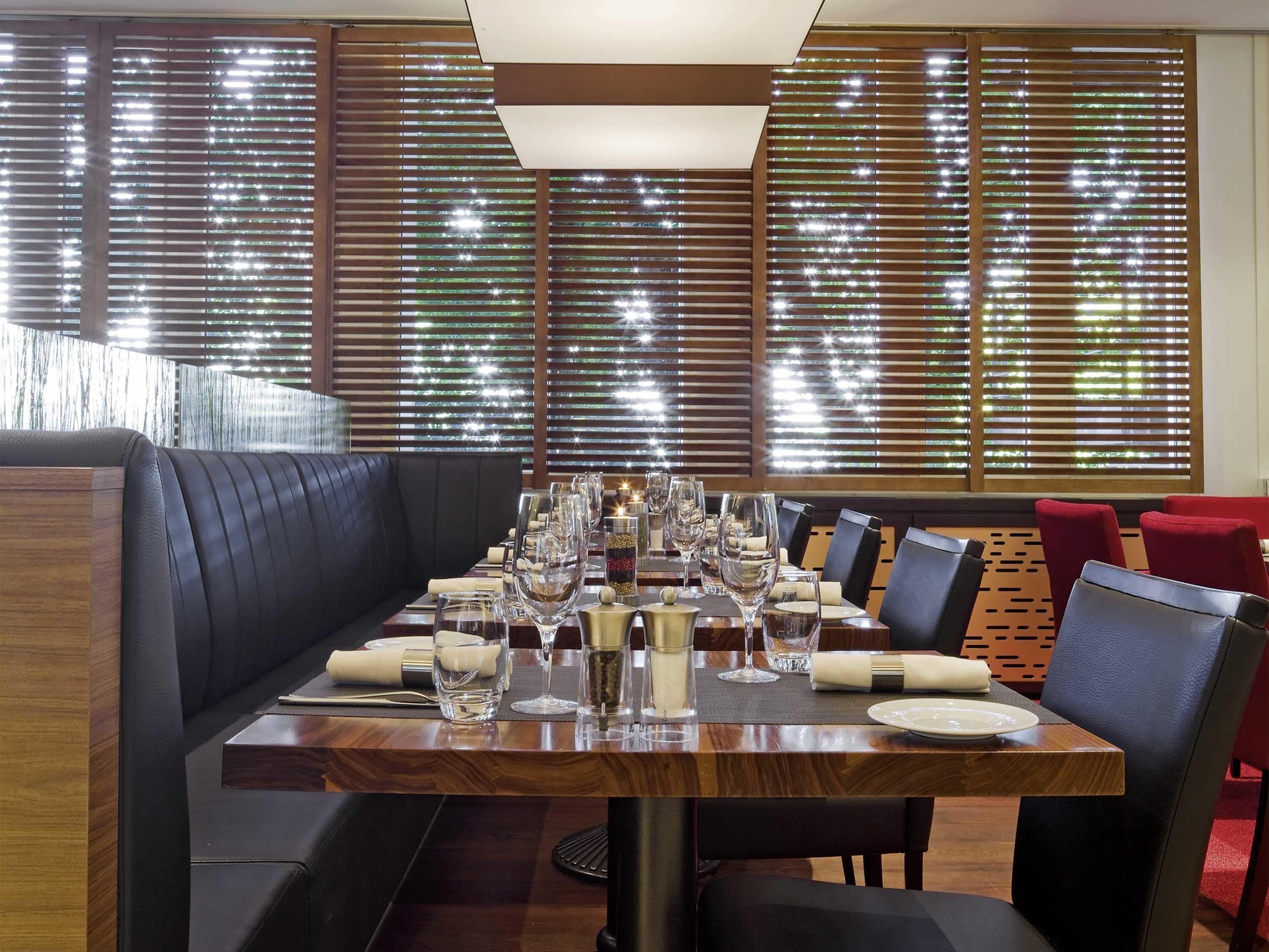A dining area with a wooden table set for a meal, surrounded by black and red upholstered chairs.