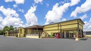 A motel with a covered parking area, a Coca-Cola vending machine, and a clear blue sky with clouds.