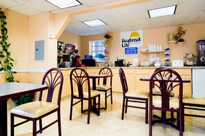 A breakfast bar with wooden chairs and tables, a sign for Daybreak Lite breakfast, and a kitchen area with appliances. - Days Inn by Wyndham Waycross (Waycross)