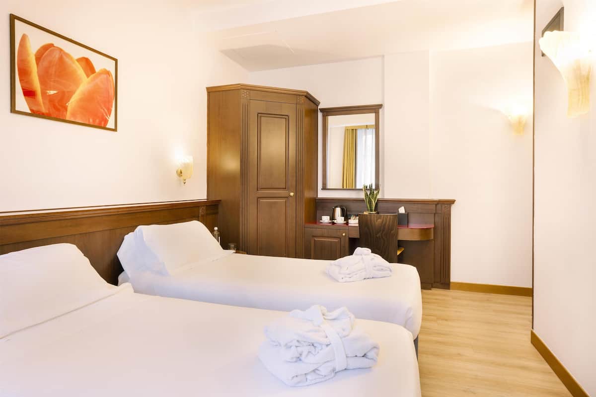 Une chambre d’hôtel avec deux lits, une armoire en bois, un bureau avec un miroir et un tableau au mur.