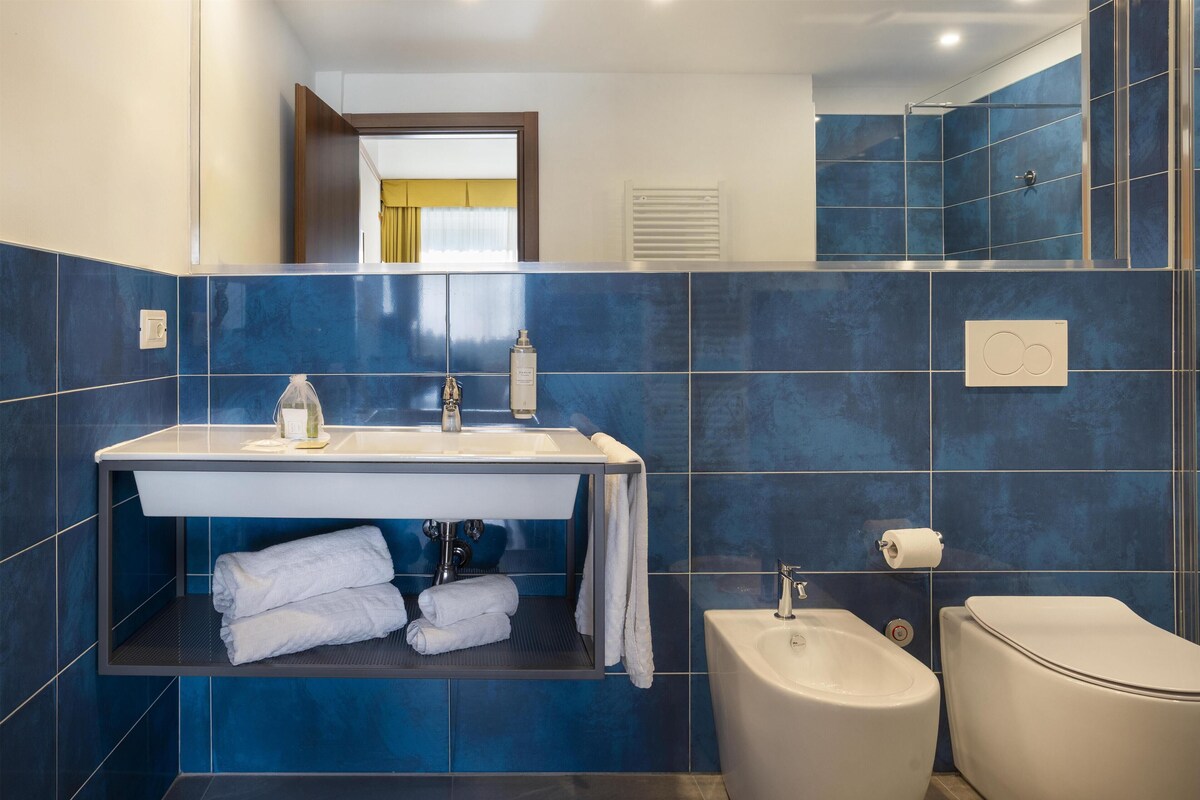Ein Badezimmer mit blauen Fliesen, einem Waschbecken, einem Spiegel, einer Toilette und einem Bidet.