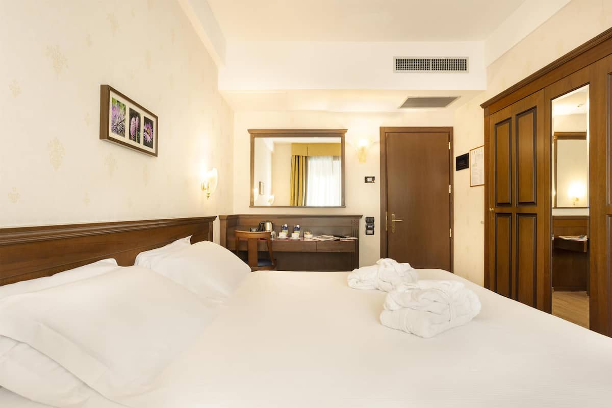 Une chambre d’hôtel avec un grand lit, un bureau, un miroir et une armoire.