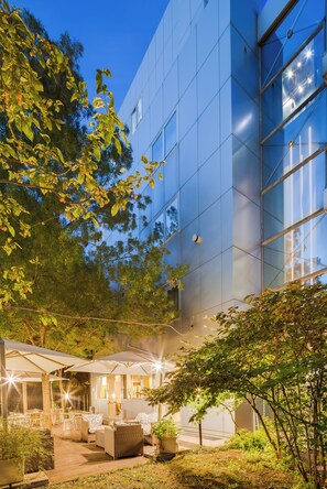 A modern building with large windows and a courtyard with outdoor seating and greenery.