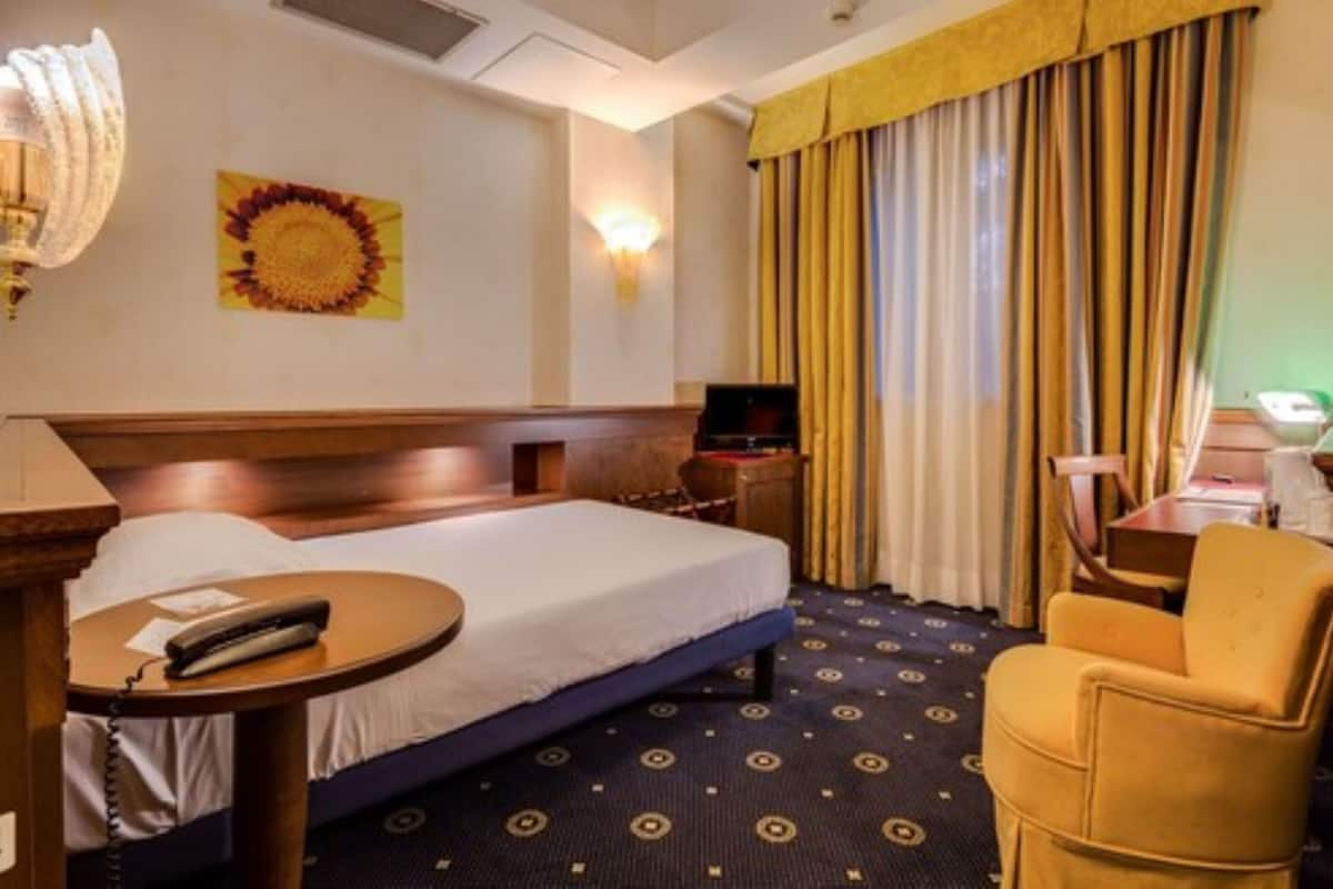 Une chambre d’hôtel équipée d’un lit, d’une chaise, d’un bureau, d’une lampe, d’un téléviseur et d’un élément décoratif mural.
