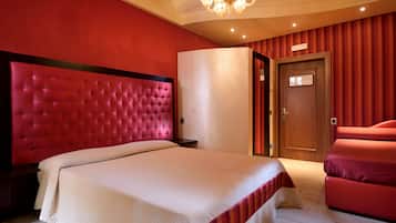 Habitación de hotel con un gran cabecero capitonado, cama con ropa de cama blanca, pared de acento roja, candelabro y puerta con placa de identificación.