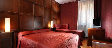 A hotel room with a large bed, two smaller beds, a TV, and a desk.