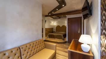 A bedroom with a bed, a sofa, a bedside table with a lamp, and a TV mounted on the wall.