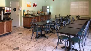 Une cafétéria avec plusieurs tables et chaises, un distributeur de boissons et un réfrigérateur.