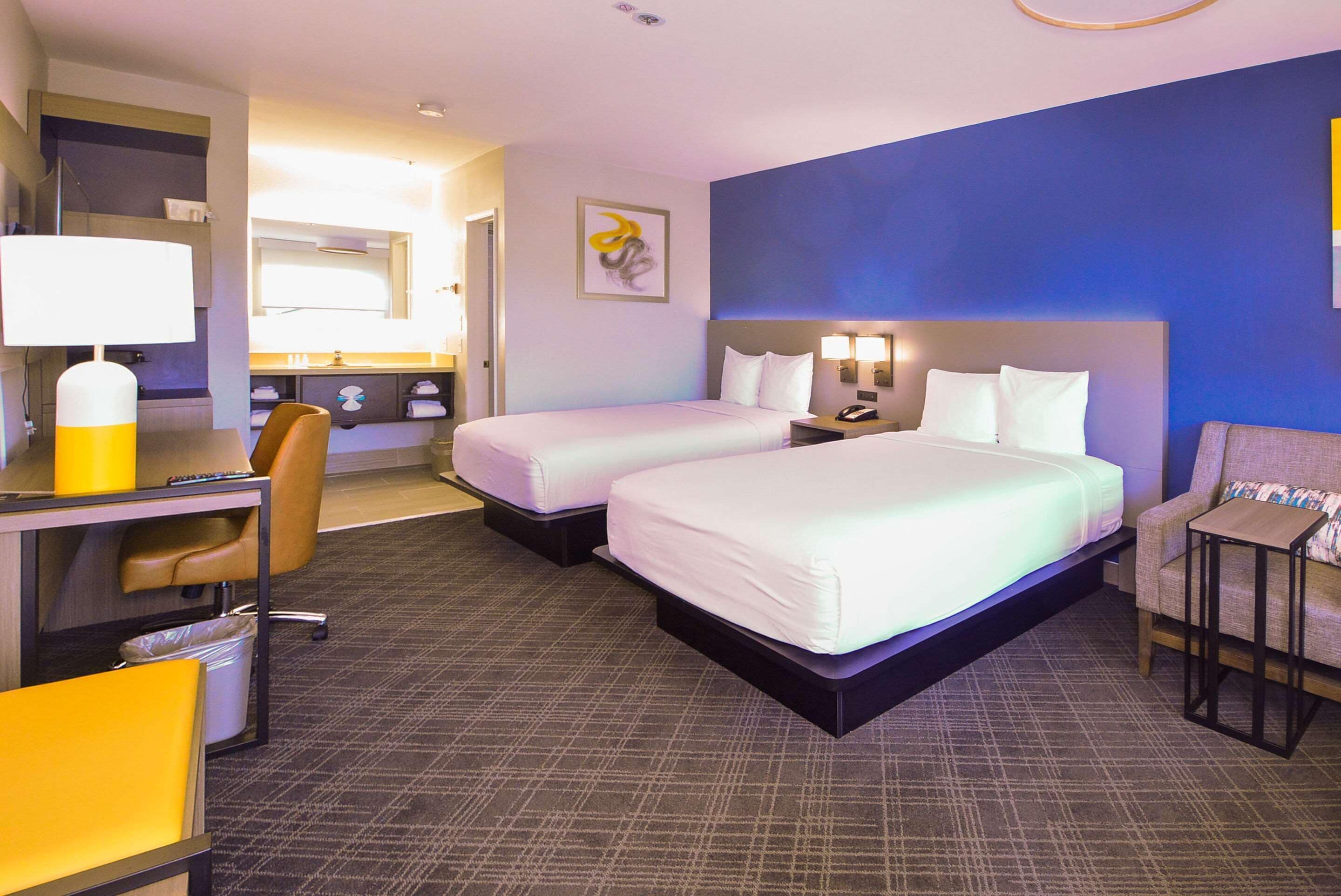 A hotel room with two beds, a desk with a chair, a small table, and a couch.