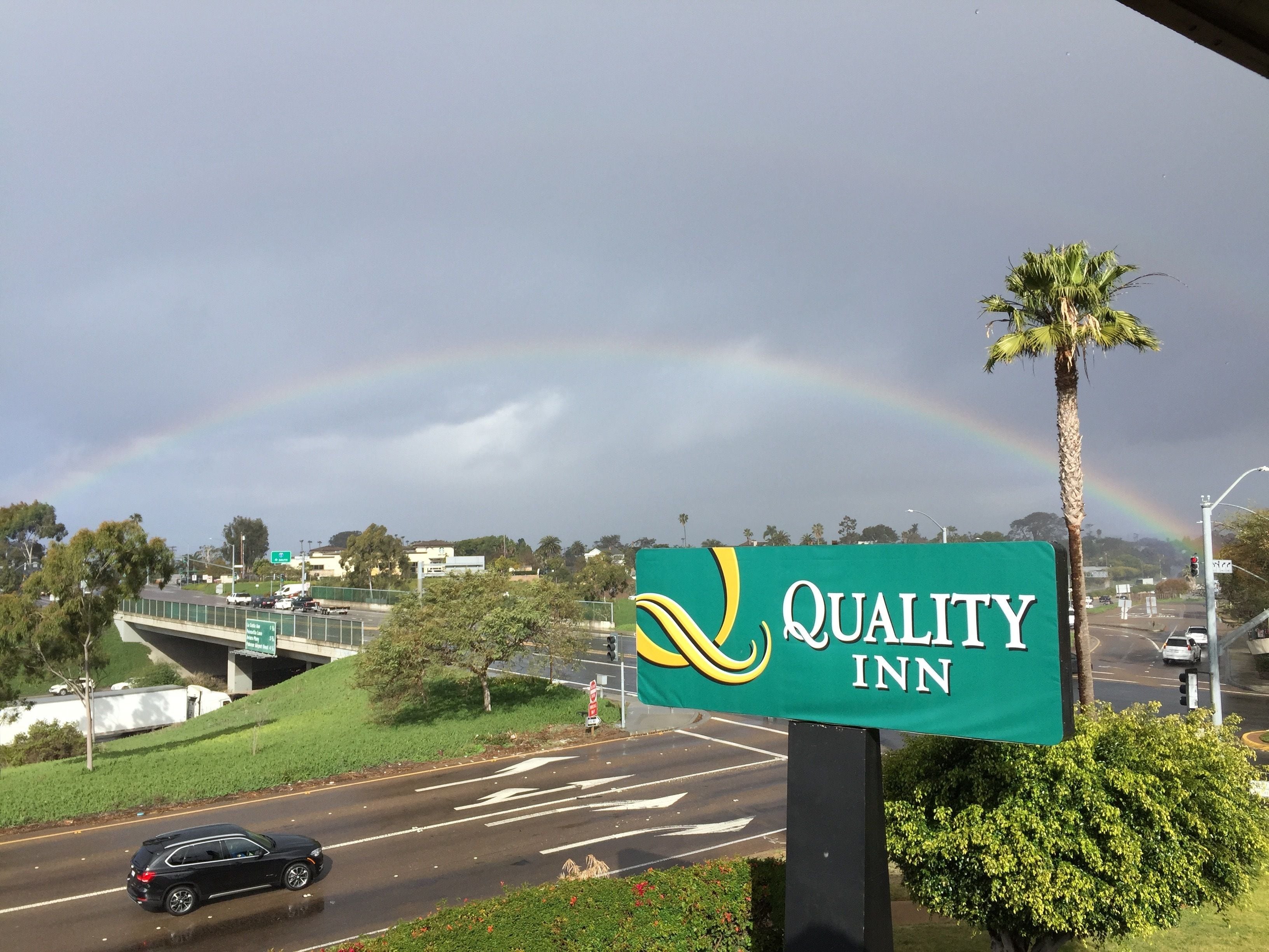 A sign for Quality Inn with a rainbow in the background.