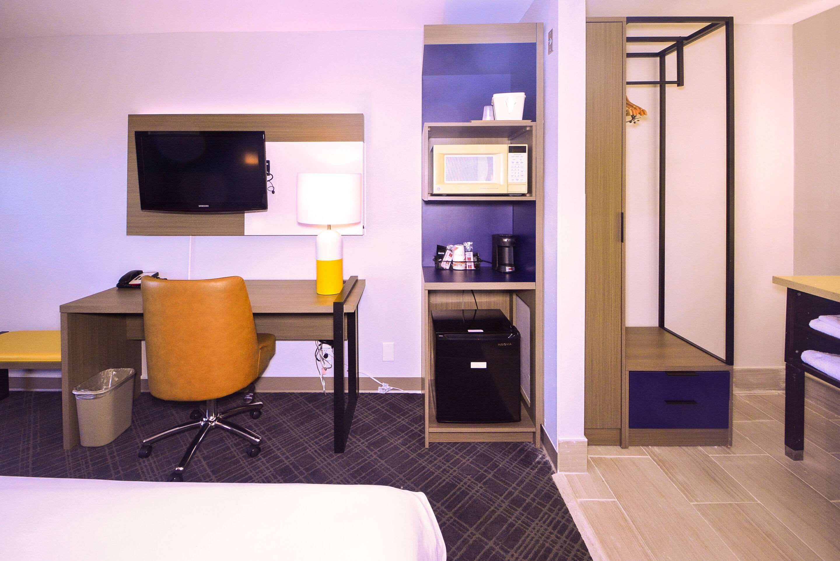 A hotel room with a bed, desk, chair, TV, microwave, and storage cabinets.