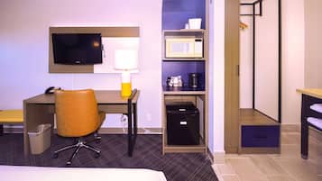 A hotel room with a bed, desk, chair, TV, microwave, and storage cabinets.