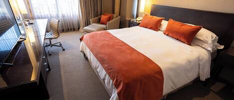 A hotel room with a large bed, a desk with a computer, a chair, and a lamp.