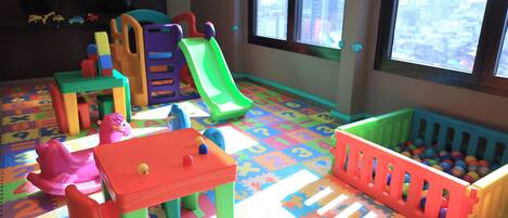 Una sala de juegos con juguetes coloridos, un tobogán y una piscina de pelotas.