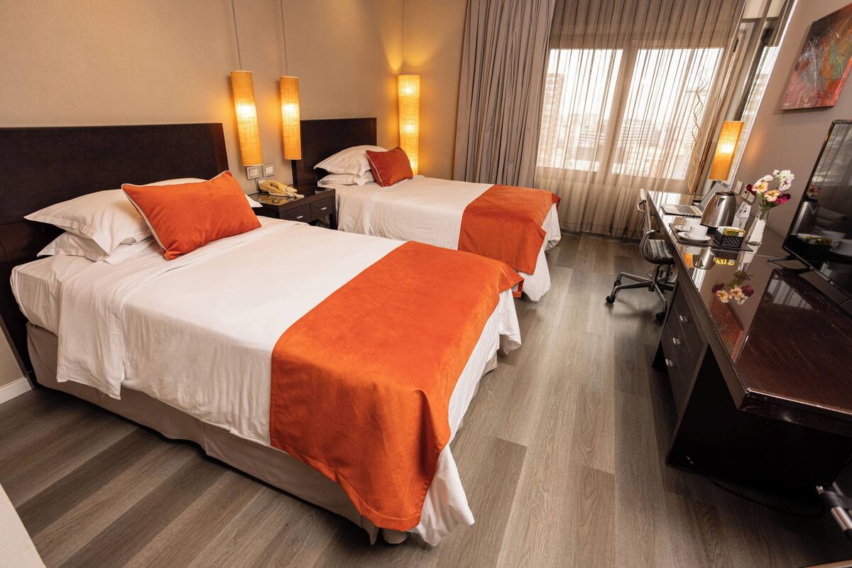 Ein Hotelzimmer mit zwei Betten, einem Schreibtisch mit Stuhl, einem Telefon und einem Fernseher.