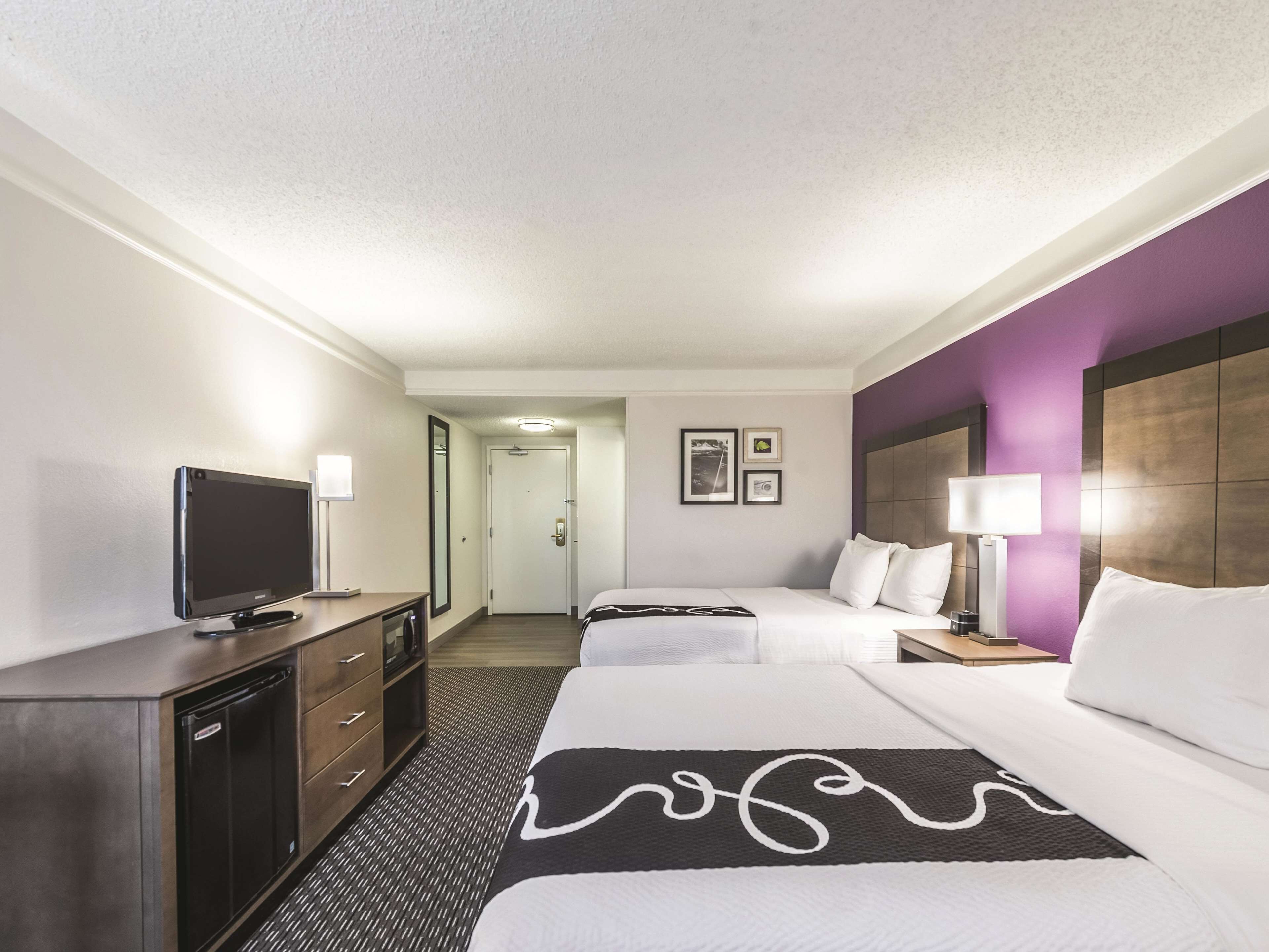 A hotel room with a bed, bedside tables, a TV, a desk, and a wardrobe.