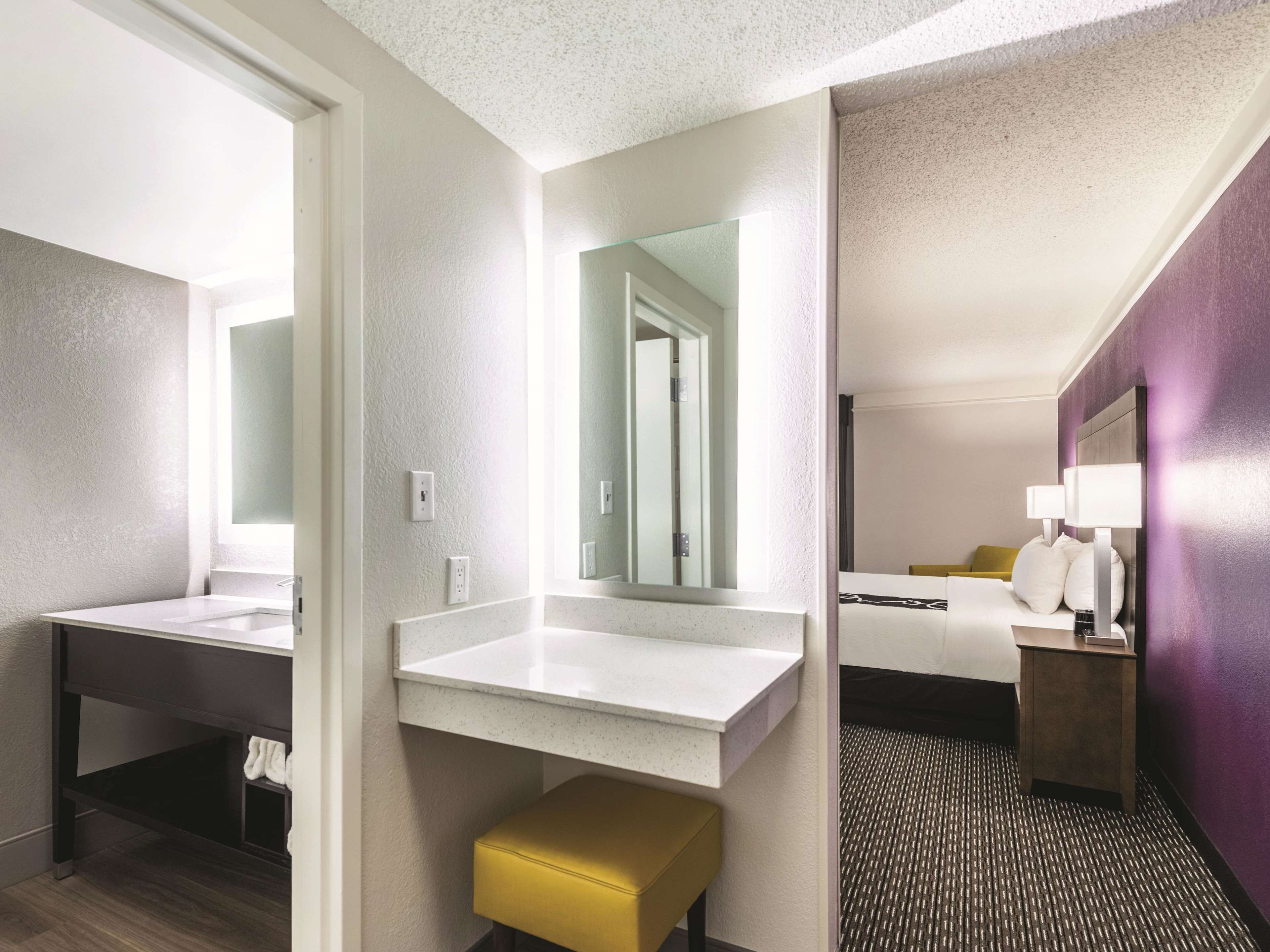 Un baño de hotel con un espejo grande, un lavamanos blanco y un banco amarillo.