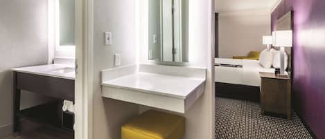 Un baño de hotel con un espejo grande, un lavamanos blanco y un banco amarillo.