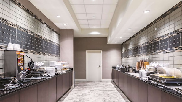 A modern kitchen with a central island, equipped with a waffle maker, coffee machine, and various food containers.