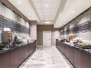 A modern kitchen with a central island, equipped with a waffle maker, coffee machine, and various food containers.