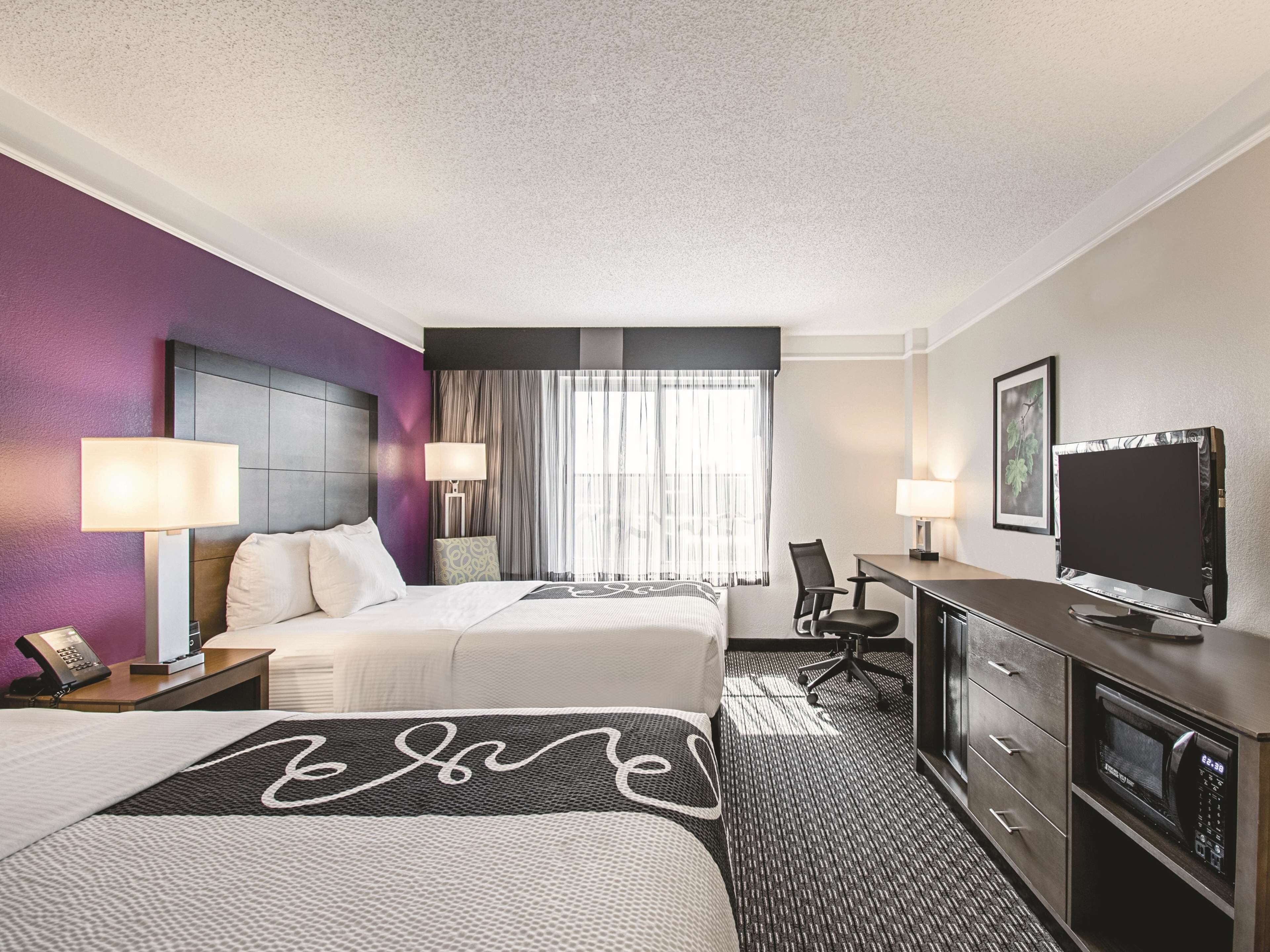 A hotel room with two beds, a desk with a TV, a microwave, and a phone on the nightstand.