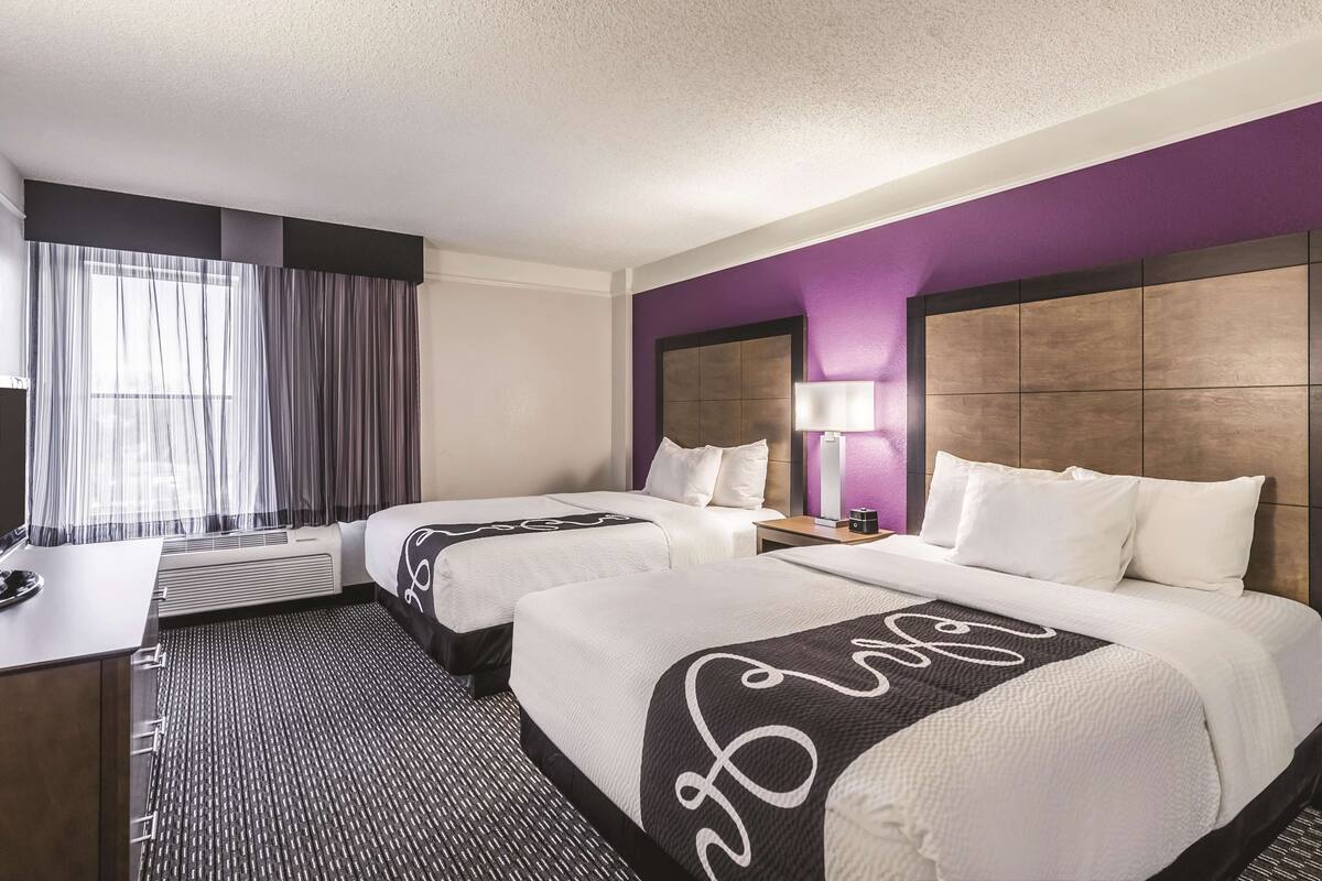 Habitación de hotel con dos camas, un escritorio y una ventana con cortinas.