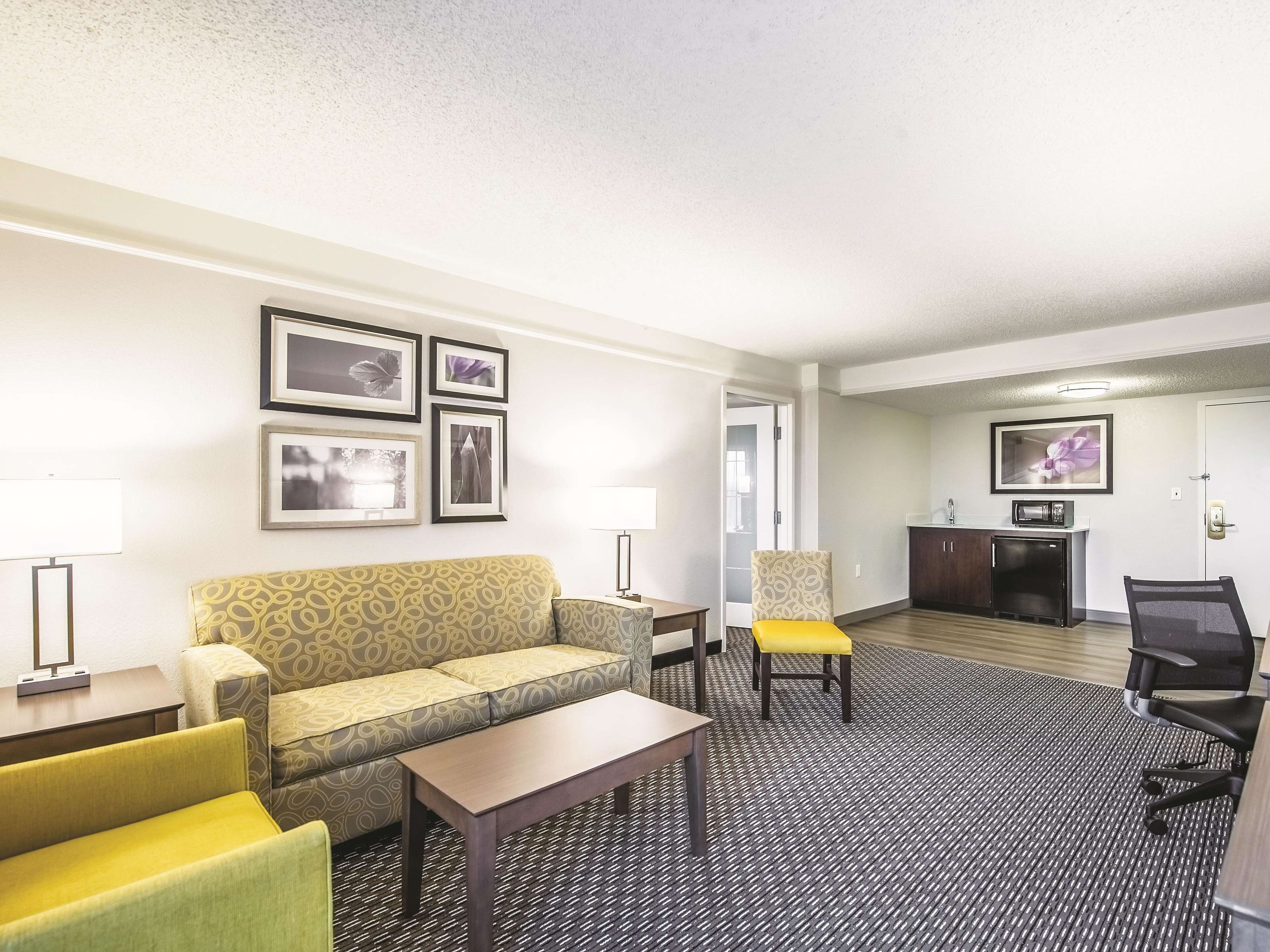 A hotel room with a sofa, armchairs, a small table, a desk, and a kitchenette area.