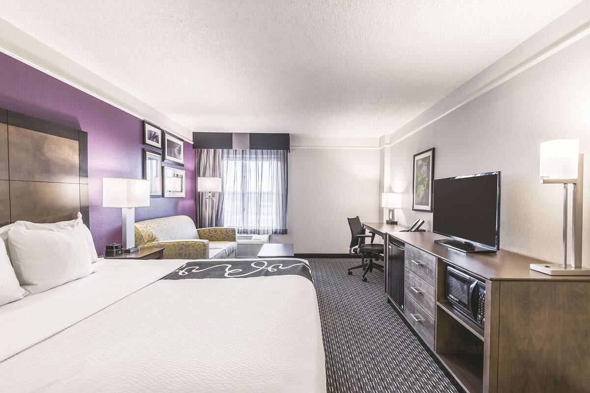Habitación de hotel con una cama grande, un escritorio con silla, televisión y un minibar.